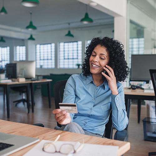 A woman is talking on the phone while looking at a credit card.