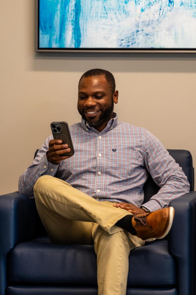 A man is sitting down and looking at his phone.